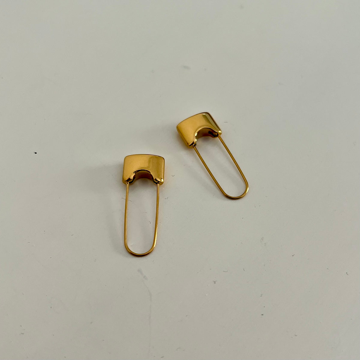 A pair of 18KT gold plated safety pin earrings on a white background.