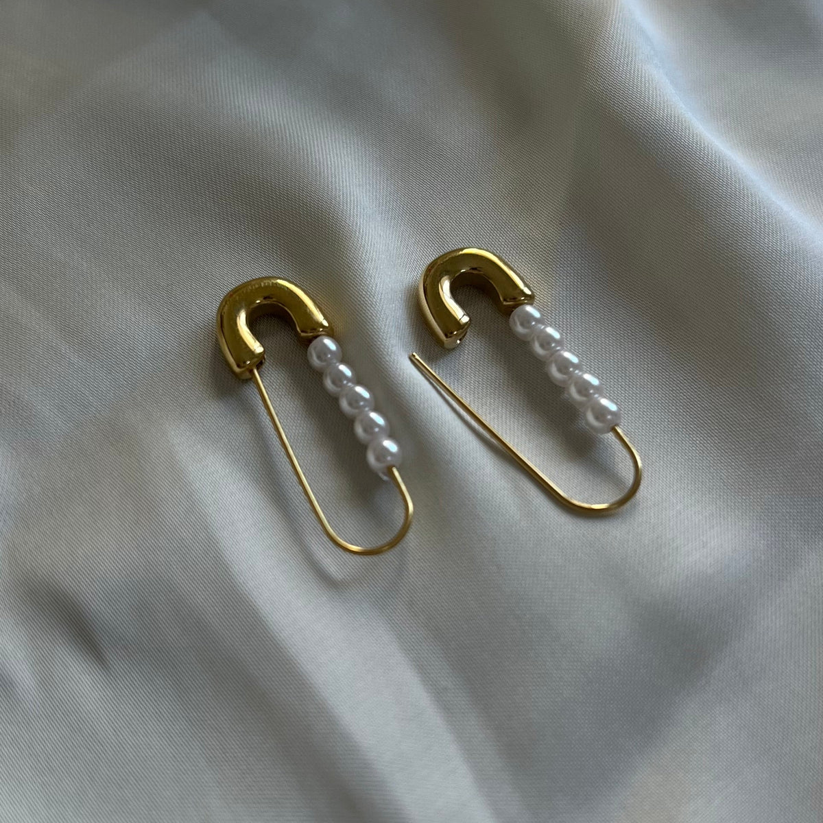 A pair of gold safety pin earrings with a row of pearls; gold pearl safety pin earrings